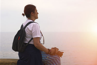 Side view of young woman standing against sea