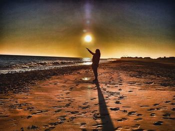 Silhouette person standing on beach against sky during sunset