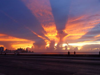 Silhouette people on beach against sky during sunset