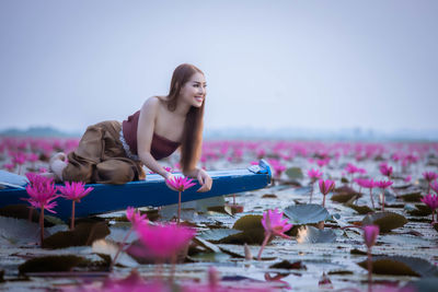 Young woman with pink flowers floating on water against sky