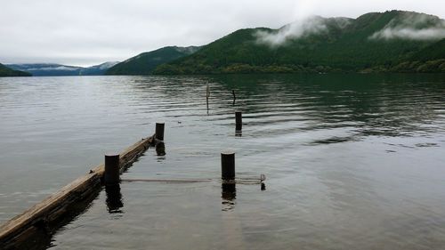 Wooden posts in lake against sky