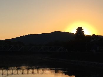 Silhouette of bridge over river at sunset