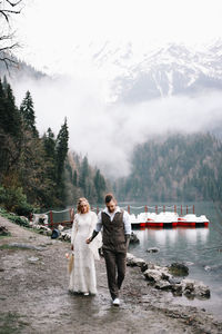 Two happy people in love the bride and groom in wedding outfits embrace by the lake and mountains
