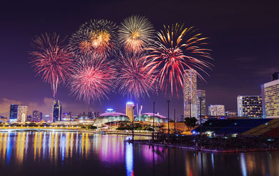 Firework display in city against sky at night