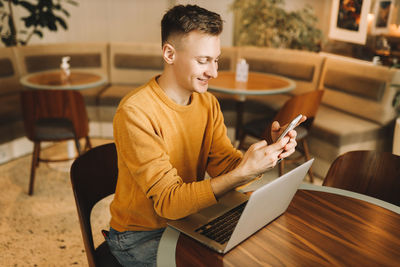 Young man using mobile phone while sitting on table