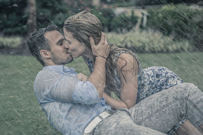 Couple kissing while sitting on grass during rain