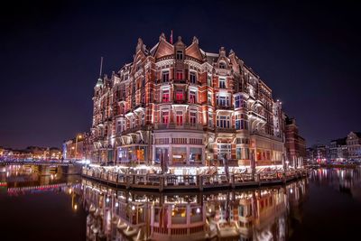 Illuminated building reflecting on lake at dusk