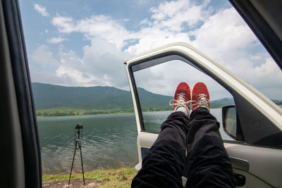 Low section of man relaxing in car against sky