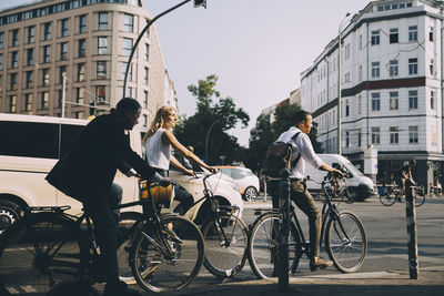 Full length of business colleagues riding bicycles against building in city