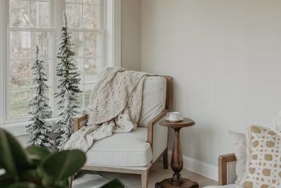 Chair with soft blanket and cup of coffee on small table in white room