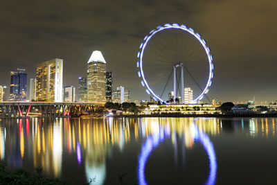 Illuminated singapore flyer by river at night
