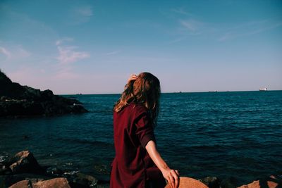 Rear view of woman standing at beach against sky