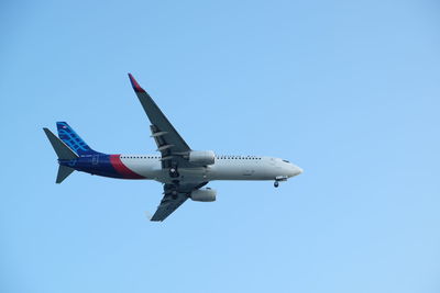 Low angle view of airplane flying against clear blue sky