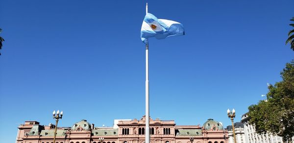 Low angle view of flag against building against clear blue sky