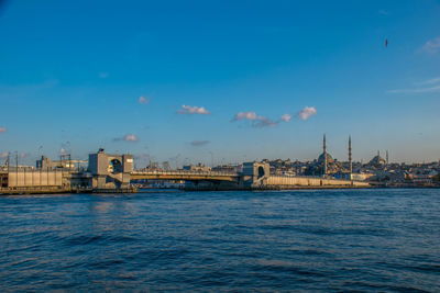 View of buildings by river against blue sky