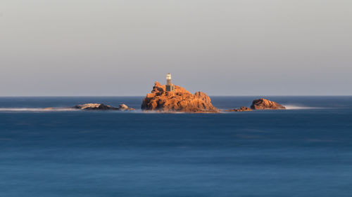 Lighthouse on rock by sea against sky