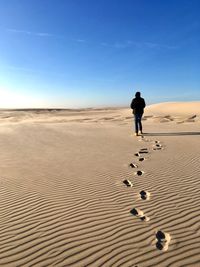 Full length rear view of person walking on sand in desert against sky