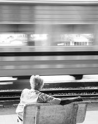 Rear view of man sitting on bench at railroad station 