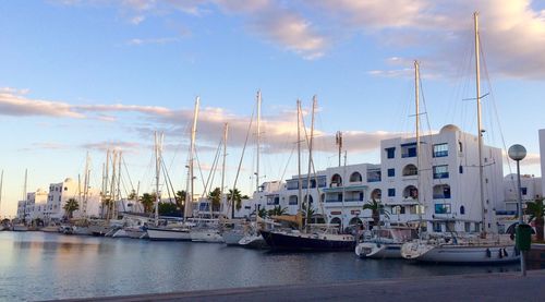 Boats moored at harbor in city against sky