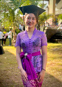 Portrait of woman wearing graduation gown standing in park