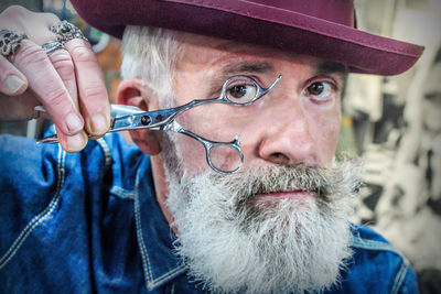 Close-up portrait of senior hipster barber holding scissors in salon