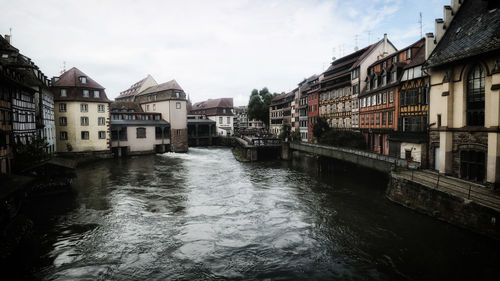 View of buildings by river against cloudy sky