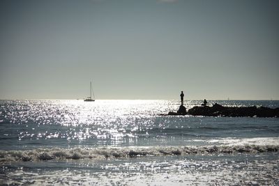 Silhouette of two people standing on rocks in sea against clear sky