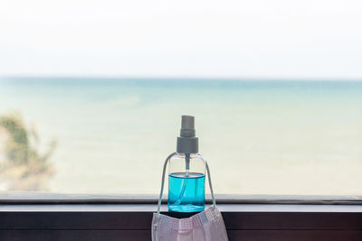 Close-up of glass bottle on table by sea against sky