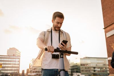 Mid adult man using smart phone while standing with electric push scooter in city