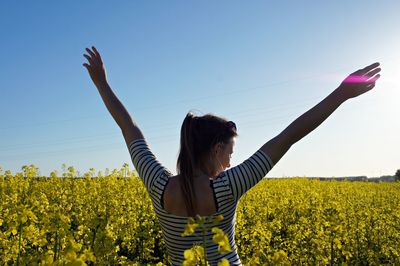 Rear view of woman standing amidst yellow flowering plants on field against sky during sunny day