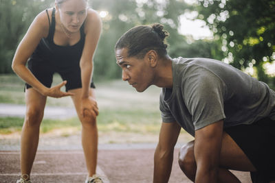 Female instructor guiding determined man preparing for sprint on running track