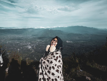 Portrait of smiling woman standing on mountain against sky