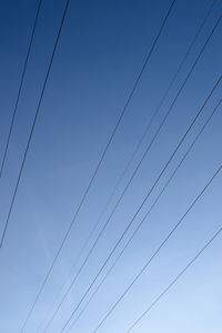 Low angle view of power cables against clear blue sky