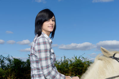 Portrait of smiling woman riding horse against sky