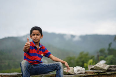 Portrait of man sitting on rock against mountains