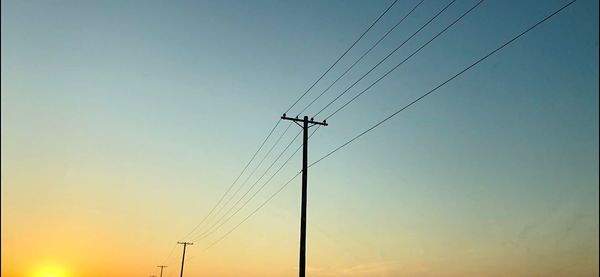 Low angle view of electricity pylon against sky during sunset