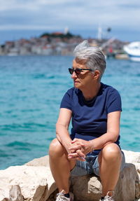 Portrait of senior woman sitting on the sea shore with mediterranean town in background