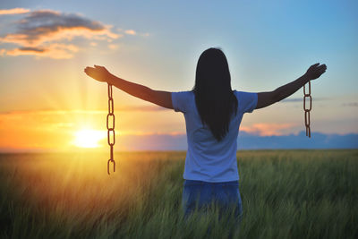 Rear view of woman standing on field against sky during sunset