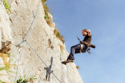 Sportive male alpinist climbing on sheer cliff in summer day