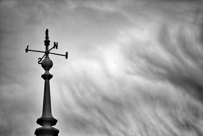 Low angle view of weather vane against cloudy sky