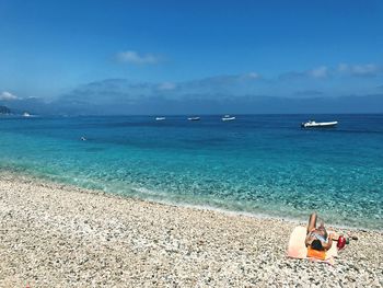 Woman relaxing on shore at beach against sky