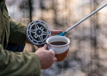 Close-up view with fisherman's hands, fishing reel and tea cup on a blurred background, fishing