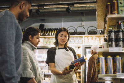 Saleswoman discussing over canned products to customers at store