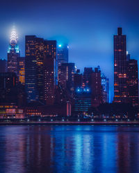 Illuminated city by river against sky at night