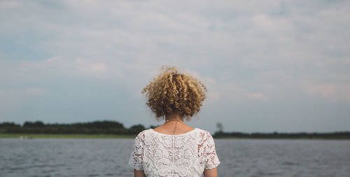 Rear view of woman standing by lake against sky