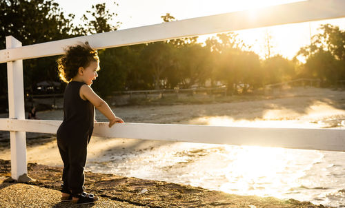 Side view of boy standing at shore against sky during sunset