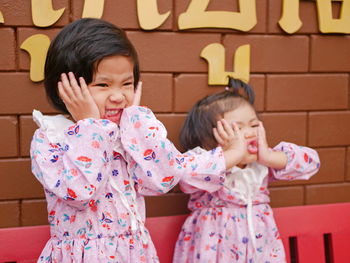 Cute girls making face standing against wall outdoors