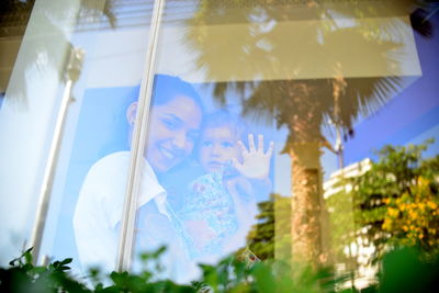 Low angle view of woman holding girl seen through glass window with reflection