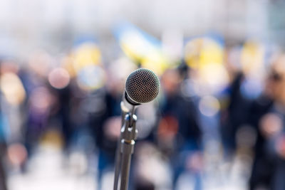 Anti-war meeting, focus on microphone, blurred crowd of people with ukrainian flags in background