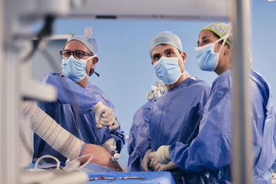 Surgeon team wearing protective face mask operating shoulder arthroscopic surgery while standing in operation room